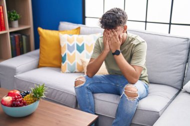 Young hispanic teenager stressed sitting on sofa at home
