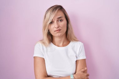 Young blonde woman standing over pink background looking sleepy and tired, exhausted for fatigue and hangover, lazy eyes in the morning. 