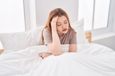 Young redhead woman stressed sitting on bed at bedroom