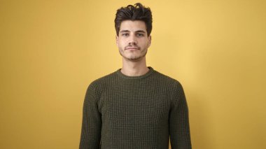 Soyutlanmış sarı arka planda ciddi bir ifadeyle duran İspanyol genç adam.