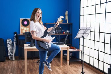 Young woman musician playing electrical guitar at music studio