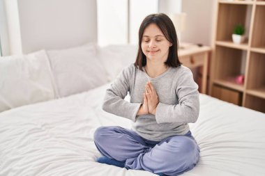 Down sendromlu genç bir kadın yatak odasında yoga egzersizi yapıyor.