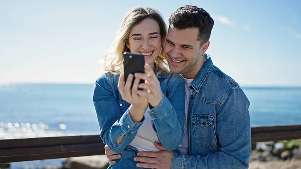 男性と女性のカップルが一緒に立っている海辺のスマートフォンを使って — ストック写真