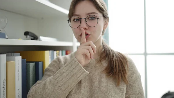 Young blonde woman student doing silence gesture at library university