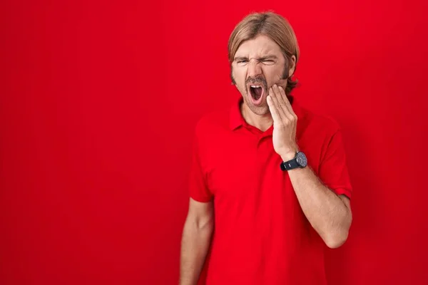Caucasian man with mustache standing over red background touching mouth with hand with painful expression because of toothache or dental illness on teeth. dentist