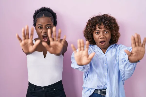 ピンクの背景に立っている2人のアフリカ人女性が手でジェスチャーを停止します — ストック写真