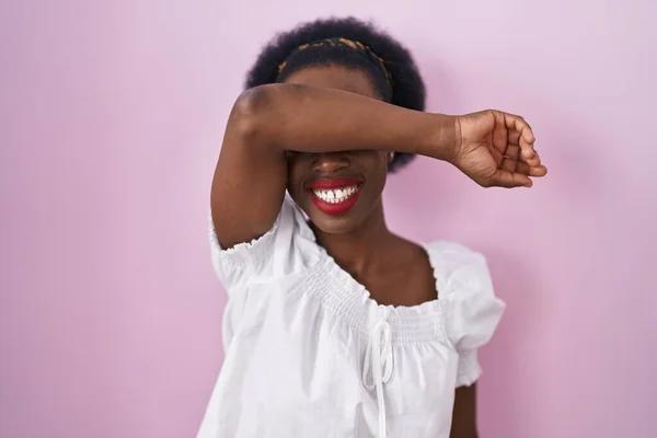 カールした髪をしたアフリカ人女性がピンクの背景の上に立ち 陽気で面白い腕で目を覆います 視覚障害の概念 — ストック写真