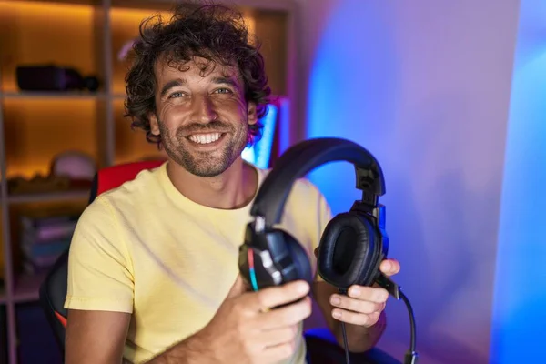 年轻的惊慌失措的男人带着自信的笑容在游戏室拿着耳机 — 图库照片