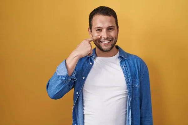 Латиноамериканець Стоїть Над Жовтим Фоном Показуючи Пальцем Обличчя Носа Усміхаючись — стокове фото