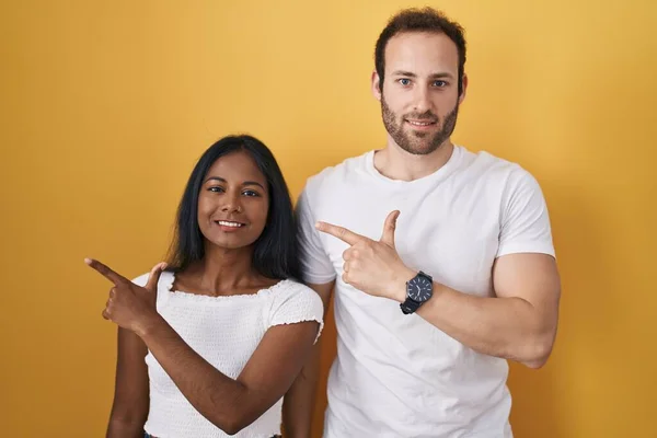 Interracial Couple Standing Yellow Background Cheerful Smile Face Pointing Hand — Stock Photo, Image
