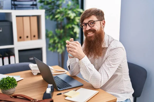 Νεαρή Κοκκινομάλλα Επιχειρηματίας Χρησιμοποιώντας Φορητό Υπολογιστή Πίνοντας Καφέ Στο Γραφείο — Φωτογραφία Αρχείου