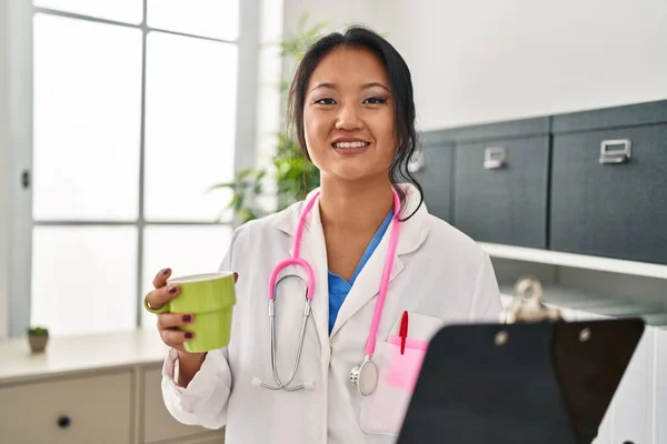 Young Chinese Woman Wearing Doctor Uniform Holding Clipboard Drinking Coffee — Fotografia de Stock