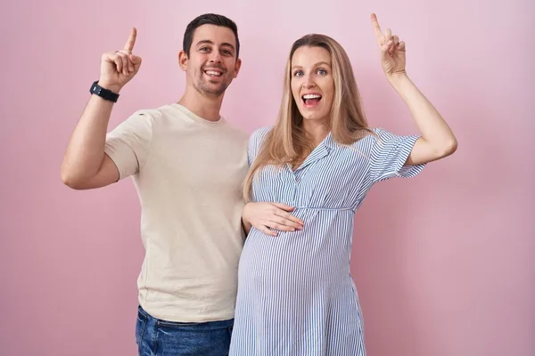 Casal Jovem Esperando Bebê Sobre Fundo Rosa Sorrindo Espantado Surpreso — Fotografia de Stock