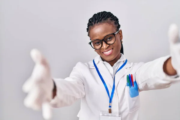 身穿科学家制服 头戴辫子的非洲女人看着摄像机 张开双臂拥抱 欢快的表达拥抱幸福 — 图库照片