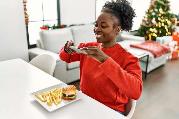 아프리카 미국인 크리스마스 식탁에 햄버거로 스마트폰으로 사진을 찍는다 — 스톡 사진