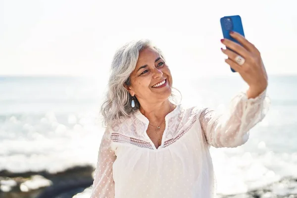 stock image Middle age woman smiling confident making selfie by the smartphone at seaside