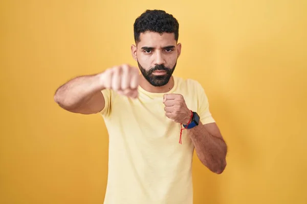 髭を生やしたヒスパニック系の男の上に立って黄色の背景パンチング拳で戦うために 積極的かつ怒っている攻撃 脅威と暴力 — ストック写真