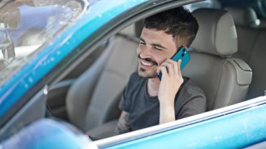 Akıllı telefondan konuşan genç bir İspanyol sokakta stresli bir şekilde arabada oturuyor.