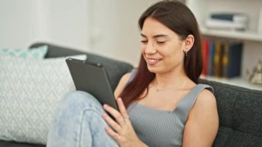 Evdeki kanepede oturan dokunmatik ped kullanan genç ve güzel İspanyol kadın.