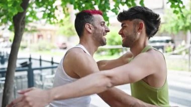 Two men couple smiling confident hugging each other at park