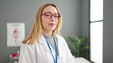 Klinikte steteskop takarak gülümseyen genç sarışın kadın doktor.