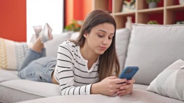 Genç, güzel, İspanyol bir kadın akıllı telefon kullanıyor. Evde üzgün görünüyor.