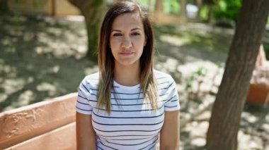 Ortadoğulu bir kadın parkta bankta otururken kendinden emin bir şekilde gülümsüyor.