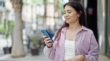 Genç, güzel, İspanyol bir kadın sokakta akıllı telefondan müzik dinliyor.