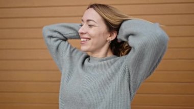 Genç sarışın kadın gülümsüyor kendinden emin elleri izole ahşap arka planda saçlarını tarıyor.