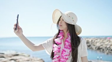 Genç Çinli kadın turist gülümsüyor. Kendine güveni tam. Deniz kenarında akıllı telefondan selfie çekiyor.