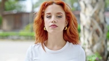 Genç kızıl saçlı kadın gülümsüyor. Parkta sessiz hareketler yapıyor.