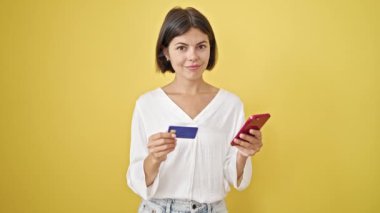 Akıllı telefon ve kredi kartıyla alışveriş yapan genç, güzel İspanyol kadın izole edilmiş sarı arka planda