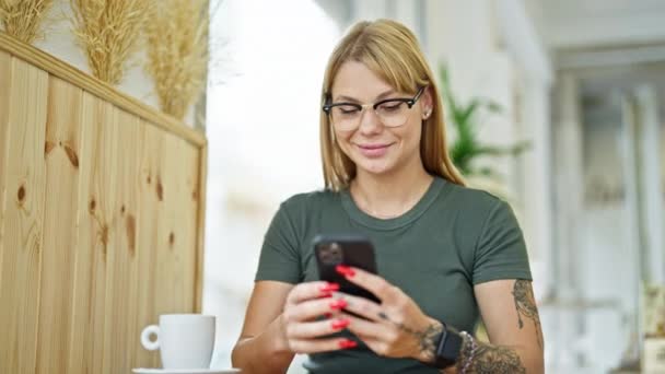 Genç Sarışın Kadın Kahve Dükkanında Gülümseyen Akıllı Telefon Kullanıyor — Stok video