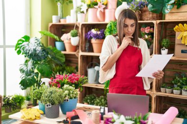 Young beautiful hispanic woman florist using laptop reading document at flower shop