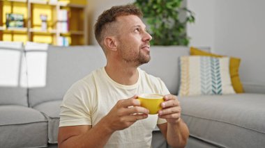 Genç adam evde yerde oturup kahve içiyor.