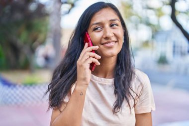 Genç, güzel, İspanyol bir kadın gülümsüyor ve caddede akıllı telefondan konuşuyor.