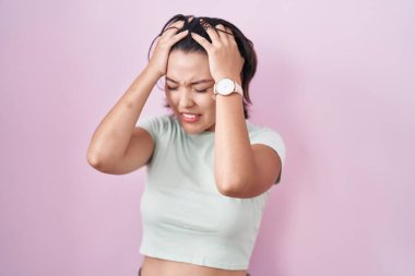 Pembe arka planda duran İspanyol genç kadın acı ve migren yüzünden çaresiz ve stresli baş ağrısından muzdarip. Eller başının üstünde.. 