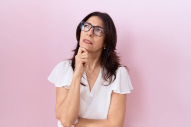 Orta yaşlı, beyaz tişört ve gözlük takan İspanyol bir kadın bir soru hakkında endişeli ve gergin bir şekilde düşünüyor. 