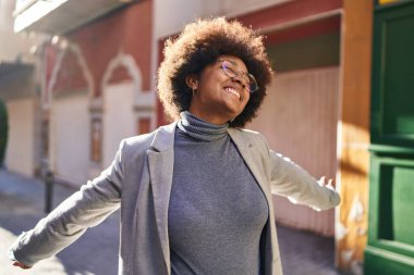 Afrikalı Amerikalı kadın yönetici. Sokakta kolları açık gülümsüyor.