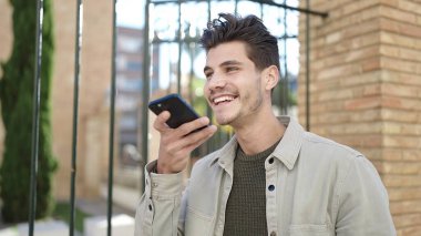 Young hispanic man smiling confident sending voice message by smartphone at street