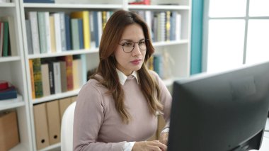 Young beautiful hispanic woman student using computer studying at library university