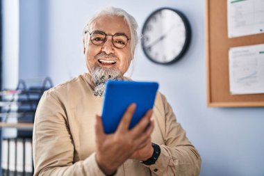 Orta yaşlı, gri saçlı iş adamı ofisteki dokunmatik pedi kullanarak gülümsüyor.