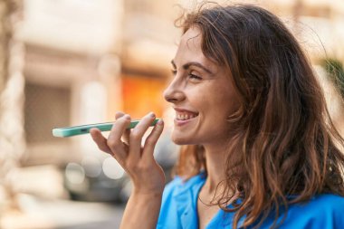 Gülümseyen genç bir kadın caddedeki akıllı telefondan konuşuyor.