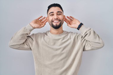 İzole edilmiş arka planda duran yakışıklı genç adam gülümsüyor parmaklarıyla kulaklarını çekiyor, komik bir jest. deneme sorunu 