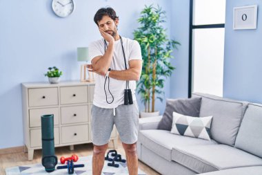 Evde spor giyinen yakışıklı Latin adam kollarını kavuşturup depresyondan sıkılmış ve yorgun görünüyor.. 