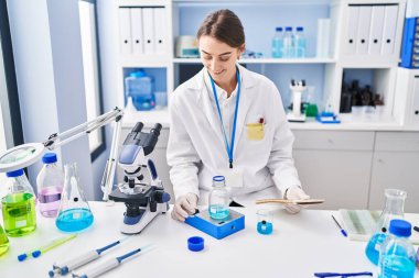 Genç beyaz kadın bilim adamı laboratuarda sıvı okuma defteri tartıyor.