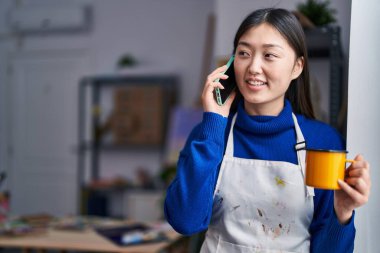 Akıllı telefondan konuşan Çinli kadın sanatçı sanat stüdyosunda kahve içiyor.