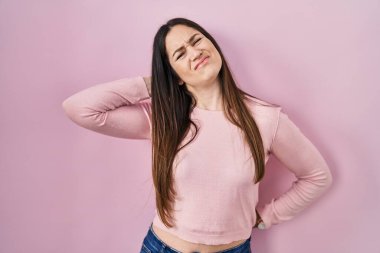 Genç esmer kadın pembe arka planda duruyor boynu ağrıyor, eli boynuna değiyor, kas ağrısı çekiyor. 