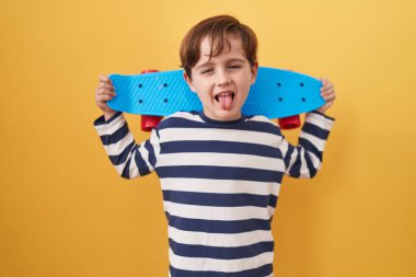 Sarı arka planda paten tutan küçük beyaz çocuk komik bir ifadeyle dilini dışarı çıkarıyor.. 