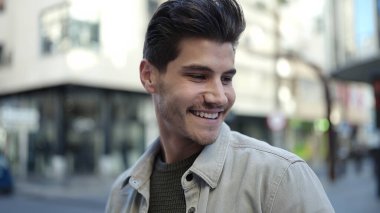 Young hispanic man smiling confident looking to the side at street